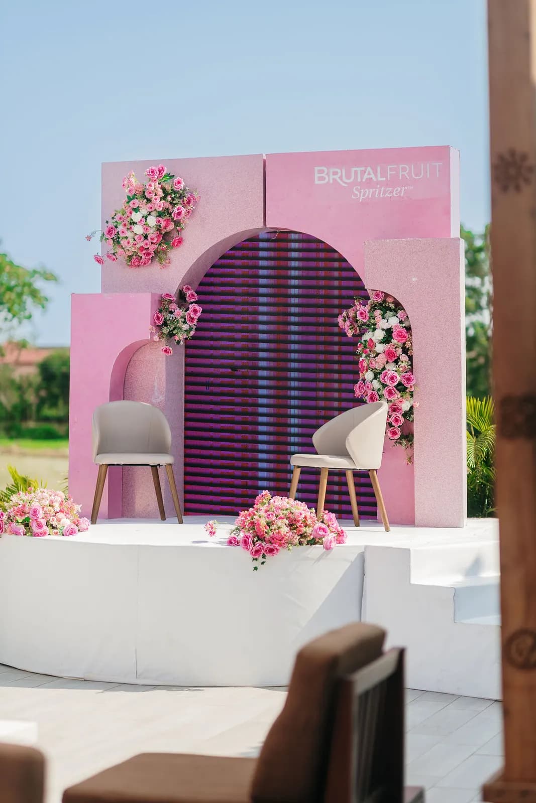 The pink stage set with an arched backdrop, two chairs and floral arrangements