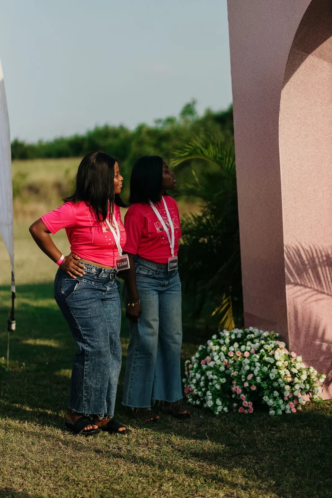 Two guests in pink tops standing on the lawn beside a flower display