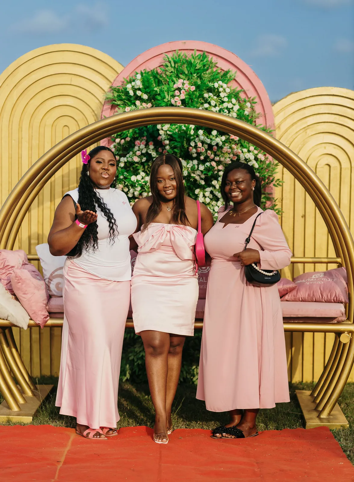 Three friends in shades of pink posing in front of the gold floral arch